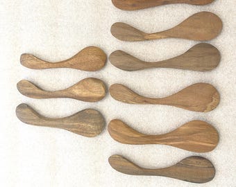 May include: A collection of eleven wooden spoons with a curved handle and a rounded bowl. The spoons are made of light brown wood and are arranged on a neutral background. The spoons vary slightly in color and grain.