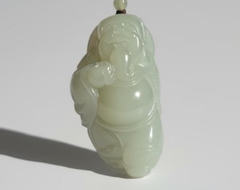 May include: A pale green jade pendant carved in the shape of a laughing Buddha. The pendant has smooth, rounded features and is suspended from a thin, light-colored cord. The Buddha is depicted with a large belly and a serene expression.