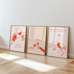 May include: Three framed art prints with a wine theme. The prints feature orange line drawings on a cream background. One says "drink o'clock", another says "cheers", and the third says "More wine, more love".