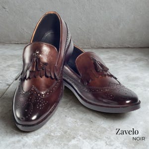 Op de afbeelding: Een paar bruine leren loafers met kwastjes en brogue details. De schoenen hebben een gepolijste afwerking en een klassiek ontwerp. De merknaam "Zavelo NOIR" is zichtbaar. Perfect voor formele gelegenheden.