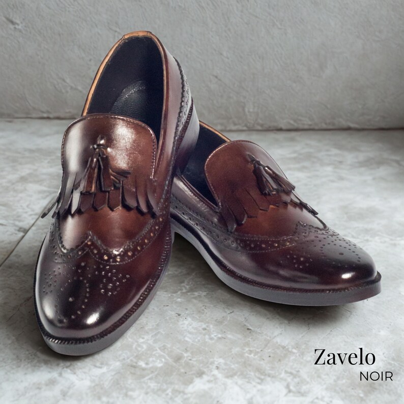 Op de afbeelding: Een paar bruine leren loafers met kwastjes en brogue details. De schoenen hebben een gepolijste afwerking en een klassiek ontwerp. De merknaam "Zavelo NOIR" is zichtbaar. Perfect voor formele gelegenheden.