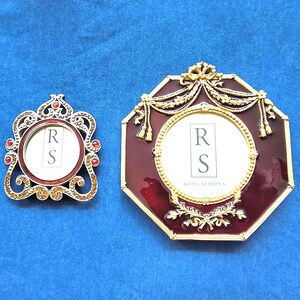 May include: Two ornate picture frames. One is small and round with red and gold accents. The other is larger, octagonal, and burgundy with gold filigree. Both have a white interior with the letters "R" and "S".