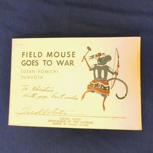 Puede incluir: Una postal vintage titulada "FIELD MOUSE GOES TO WAR" con una ilustración de un guerrero ratón sosteniendo un arco y flechas. La tarjeta incluye texto, una firma y el logotipo de la Oficina de Asuntos Indígenas del Departamento del Interior de EE. UU.