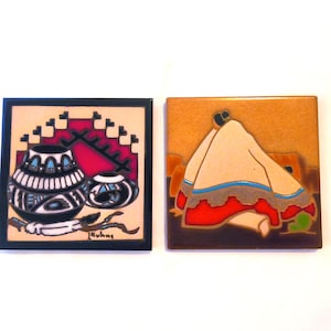 May include: Two square ceramic tiles featuring artistic designs. The left tile displays two black and white patterned pots with a red geometric background and a white feather. The right tile shows a draped cream-colored fabric with red and blue trim.