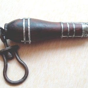 Può includere: Un manico marrone scuro con dettagli argentati e un anello di metallo. Il manico ha una forma cilindrica con bande argentate e un anello all'estremità. L'oggetto sembra essere uno strumento o parte di un meccanismo.