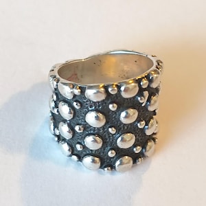 May include: A wide silver ring featuring a dark, oxidized, textured background contrasted with numerous raised, polished, smooth silver dots of varying sizes scattered across the entire outer surface of the band.