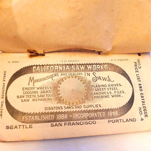 May include: A vintage 1903 California Saw Works price list and catalogue booklet. The off-white cover features black text and a central circular saw blade graphic, listing locations in Seattle, San Francisco, and Portland with aged paper.