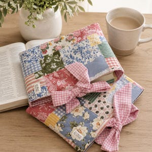Può includere: Due copertine per libri in tessuto trapuntato con un design patchwork di motivi floreali, a quadretti vichy e a righe nei toni del rosa, blu, verde e giallo. Ogni copertina include una chiusura a fiocco in tessuto vichy rosa e bianco e un'etichetta KESMADE.