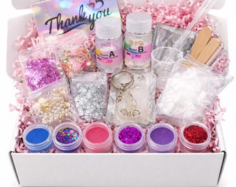 Può includere: Un kit per il fai da te in una scatola bianca contenente due flaconi etichettati A e B, sei vasetti di glitter colorati, bustine di paillettes, perle e ciondoli a forma di stella, un portachiavi in metallo e un biglietto Thank you olografico.