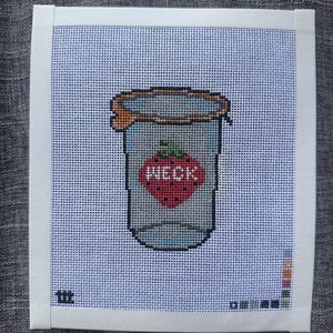 May include: A needlepoint canvas featuring a cross-stitched design of a glass jar with an orange rim. The jar has a red strawberry graphic on the front with the white text WECK printed across it. The canvas is bordered by white tape.