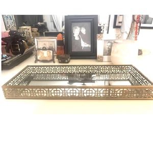May include: A rectangular decorative tray featuring a mirrored base and a metallic gold-toned frame with an intricate, repeating geometric lattice pattern along all four sides. The tray has a low profile and a reflective surface.