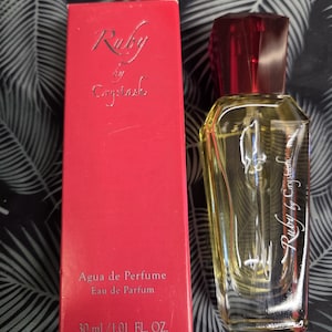 May include: A 30 ml / 1.01 fl. oz. bottle of Ruby by Crystash Eau de Parfum with a faceted red cap and golden liquid, accompanied by its matching rectangular red box featuring the product name and volume printed in silver lettering.