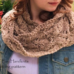 Peut inclure: Une écharpe en tricot marron infinie avec un motif en dentelle. L'écharpe est portée par une personne portant une veste en jean et une chemise blanche. Le texte "Cardiff Bay Handknits knitting pattern" est visible en bas de l'image.