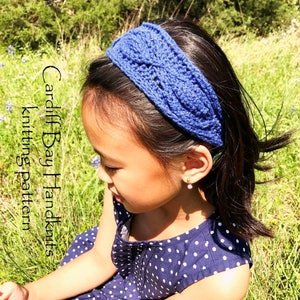 Puede incluir: Una diadema azul tejida con un delicado patrón de punto. La diadema la lleva puesta una persona joven con el pelo oscuro y un vestido de lunares.