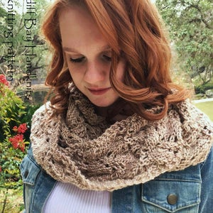Könnte beinhalten: Eine Frau trägt einen braunen und beigefarbenen gestrickten Infinity-Schal mit einem Zopfmuster. Der Schal wird über einem weißen Hemd und einer Jeansjacke getragen. Der Text "Cardiff Bay Handknits knitting pattern" ist im Bild sichtbar.