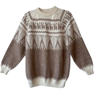 May include: A long-sleeve crew neck sweater featuring a two-tone color scheme of cream and light brown. The upper chest and shoulders display a repeating pattern of stylized llamas and geometric tree motifs, with solid ribbed cuffs and hem.