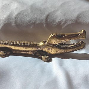 May include: A white ceramic mug with a black handle and the text "But First, Coffee" in a handwritten style. The mug is on a white surface. The mug is likely for hot beverages.