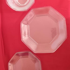May include: Three clear, octagonal glass dishes of varying sizes are arranged on a red background. The dishes have a textured surface and are likely for serving food. The arrangement suggests a set of serving dishes.