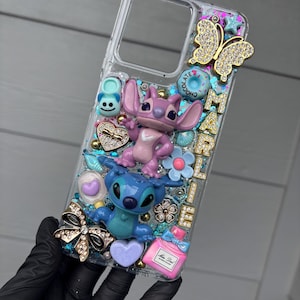 May include: Clear phone case decorated with Stitch and Angel figurines, a gold butterfly, and various embellishments. The case features the name "MARIEL" in gold letters, along with hearts, flowers, and a perfume bottle.