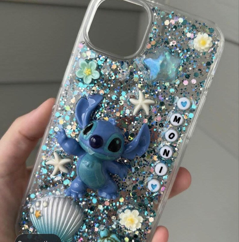 May include: Clear phone case with a blue Stitch figure, glitter, and decorative elements. The case features a blue Stitch figurine, starfish, flowers, and the word "MONI" spelled out with letter beads. The case is filled with blue and silver glitter.