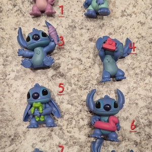 May include: A collection of eight small, colorful Stitch figurines. The figurines are in various poses, some holding accessories like ice cream cones and cameras. The color palette includes shades of blue, pink, and green.