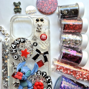 May include: Clear phone case decorated with glitter, charms, and a Stitch figurine. The case features the word "OHANA" and "STITCH" in black letters, along with a red star, bow, and flower. Several containers of glitter and beads are also visible.