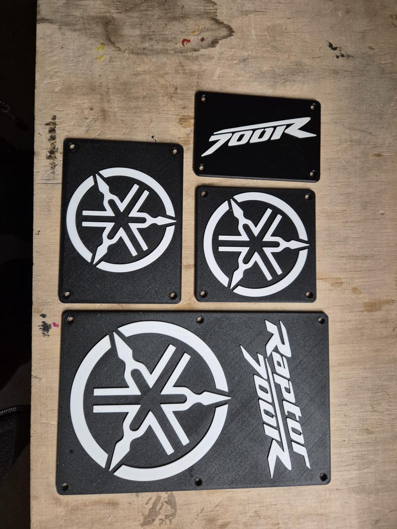 May include: A selection of black rectangular plates with white graphics. The plates display the Yamaha logo and the text "700R" and "Raptor 700R". These plates are likely for a motorcycle or ATV.