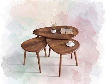 May include: A set of three wooden nesting tables with a warm brown finish. The tables have a unique, organic shape and tapered legs. A small white ceramic pot with dried flowers, a stack of books, and a teacup and saucer are on the tables.