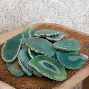 May include: A pile of polished, teal agate slices with white and brown edges. The slices are displayed on a wooden tray, highlighting their natural patterns and textures. These decorative stones are suitable for home decor or craft projects.
