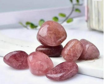 May include: A collection of polished strawberry quartz stones in varying shades of pink and red. The stones are smooth, rounded, and appear translucent, with a glossy finish. They are arranged on a white surface.