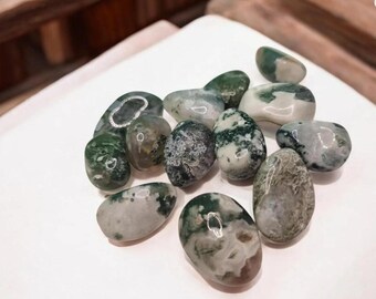 May include: A collection of polished moss agate stones. The stones vary in size and shape, with a mix of green, white, and gray colors. The moss agate stones are smooth and have a natural, organic appearance.
