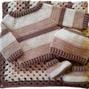 Può includere: Un set per neonati all'uncinetto fatto a mano nei toni del marrone e del crema. Il set comprende una coperta, un maglione, un cappello e delle scarpine. La coperta presenta un motivo a granny square, mentre gli altri articoli hanno motivi a righe.