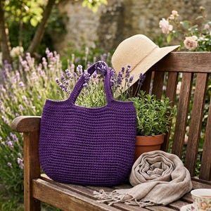 Peut inclure: Un sac fourre-tout en crochet violet foncé avec deux anses, un chapeau de soleil en paille beige, une écharpe en lin marron clair roulée avec des bords frangés et une petite plante verte en pot, disposés sur un banc en bois dans un jardin.