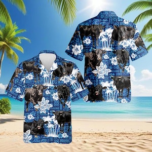 May include: Two short-sleeved button-down shirts with a blue background featuring black cows, white flowers, and palm trees. The shirts are displayed on a beach with palm trees and the ocean in the background.