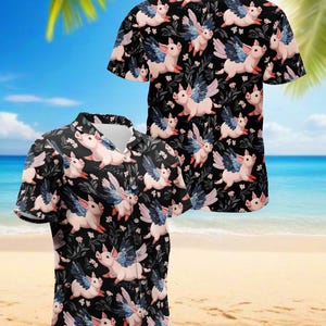 May include: Two short-sleeved button-down shirts with a black background and a repeating pattern of pink pigs with blue and white wings. The shirts are on a beach with palm trees and the ocean in the background.