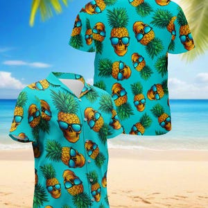 Può includere: Una camicia a maniche corte con sfondo turchese. Presenta un motivo ripetuto di ananas con facce di teschio che indossano occhiali da sole blu. La camicia ha un colletto classico e una vestibilità rilassata.