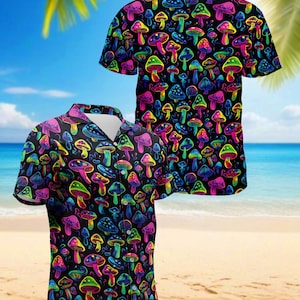 Puede incluir: Una camisa de manga corta con un estampado de setas multicolores sobre un fondo negro. Las setas son de color rosa, verde, amarillo y azul. La camisa se muestra sobre un fondo de playa.