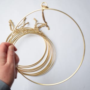 May include: A set of eight gold metal hoops of varying sizes, with a small loop at the top of the largest hoop. The hoops are stacked together and held in a hand.