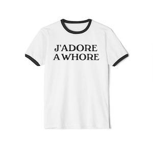 May include: White t-shirt with black trim around the collar and sleeves. The text "J'ADORE A WHORE" is printed in bold black letters on the front. A casual style t-shirt.