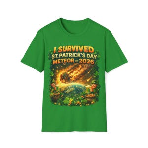 Puede incluir: Camiseta verde con el texto "I Survived St. Patrick's Day Meteor of 2026". El gráfico presenta un meteorito, la Tierra y duendes con cerveza. El diseño está rodeado de tréboles y monedas de oro.