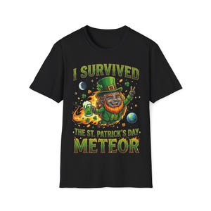 Puede incluir: Camiseta negra con un gráfico colorido que presenta un duende sosteniendo una cerveza, usando un sombrero verde y el texto "I Survived The St. Patrick's Day Meteor."