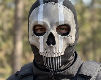 Op de afbeelding: Een zwarte bivakmuts met een gevormd, realistisch schedelmasker. De schedel is lichtgrijs met diepzwarte oogkassen en neusholte, geaccentueerd door verticale witte strepen die van het voorhoofd tot aan de kaak en kin lopen.