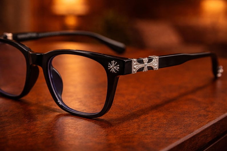 May include: Black eyeglasses with a rectangular frame and silver decorative accents. The temples feature ornate silver embellishments. The lenses are clear, and the glasses sit on a wooden surface.