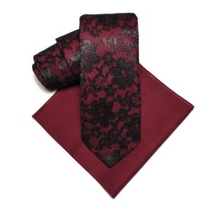 May include: A burgundy necktie with a black floral pattern and a matching burgundy pocket square.