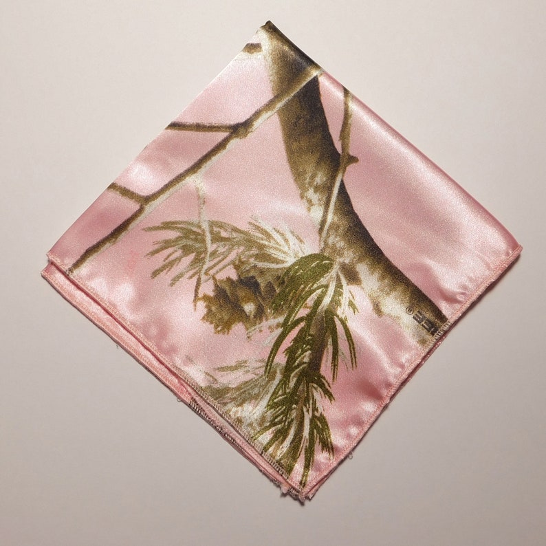 May include: Pink satin fabric with a camouflage pattern of brown branches and green leaves.