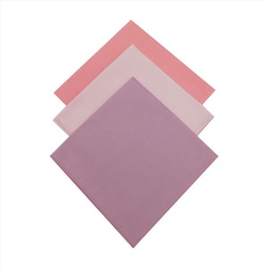 May include: Three square fabric napkins in shades of pink, light pink, and purple.