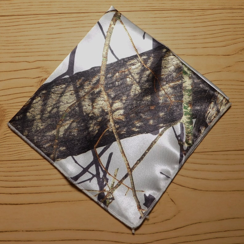 May include: A white and brown camouflage patterned pocket square. The pattern features a large tree trunk and branches.
