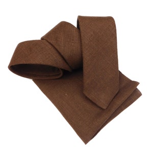 May include: A brown linen tie and pocket square set. The tie is folded in half and the pocket square is folded in thirds.