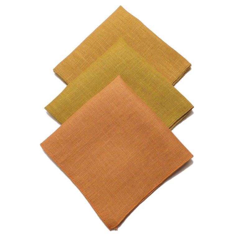 May include: Three square fabric napkins in shades of orange and yellow. The napkins are folded in thirds and stacked on top of each other.