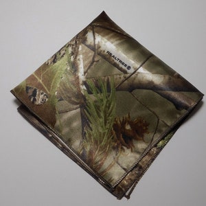 May include: A brown and green camouflage patterned fabric square with the text "REALTREE&reg;" printed in black.